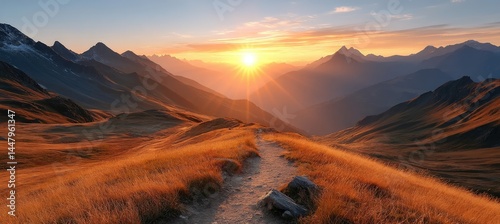 A scenic mountain landscape at sunrise, with a winding path through golden grass and sun rays lighting up the peaks.