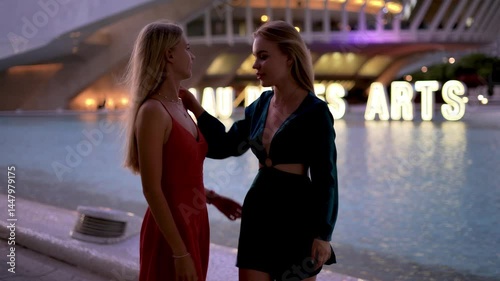 Two friendly girls in dress walking in the city full of cafes and laughing together, sunset