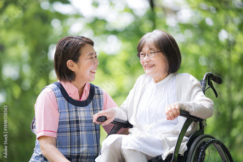 Photography A caregiver and an elderly person look at each other and smile as they stroll through the greenery