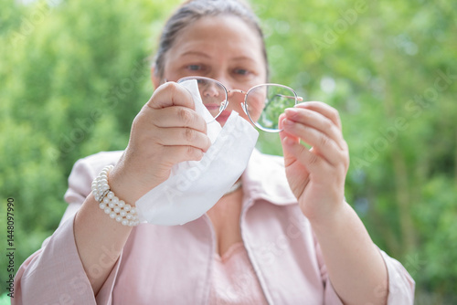 mature lady wipes spectacles, middle-aged businesswoman uses cloth to clean glasses, Clear vision, sharp mind, representing meticulous care