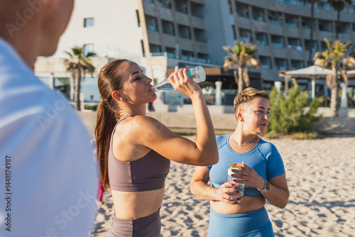 Yoga group hydrating after beach workout session - Women drinking water and relaxing after yoga class. Concept of yoga, hydration, active lifestyle.