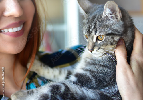 A happy woman smiles while holding her beloved tabby cat in a close-up indoor portrait, highlighting their close bond.