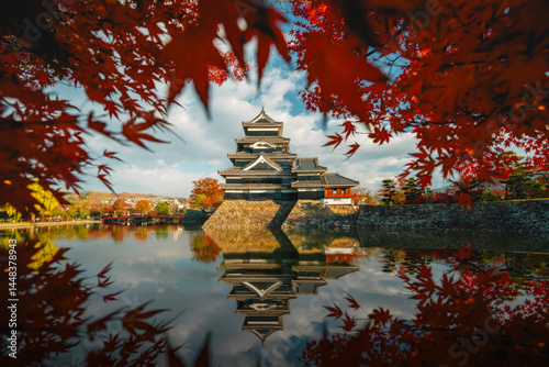 Matsumoto Castle in autumn with red maple leaves on a clear day. Crow Castle, Matsumoto City, Nagano Prefecture, Japan. Matsumoto Castle Reflection on water.