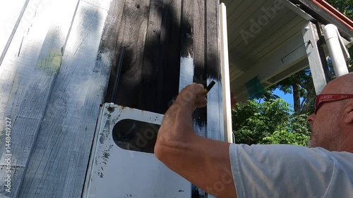 Closeup of man painting wooden cottage in countryside