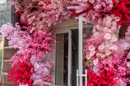 Fototapeta Naklejka Na Ścianę i Meble -  Decorating the entrance group of a store or cafe with artificial plants. Pink and flowers. Flowers around the front door