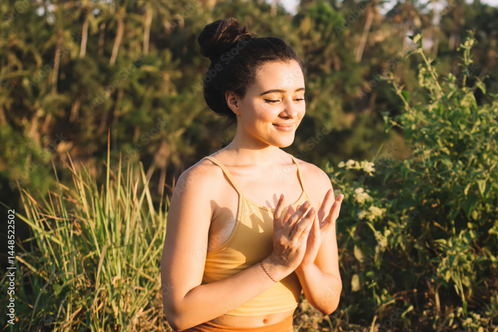 Cheerful female in active wear sitting on field recreating and feeling harmony on spiritual meditation, positive woman 20s in active wear relaxing in lotus pose keeping mental health and wellness