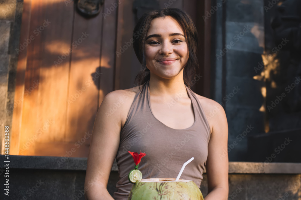 Half length portrait of positive caucasian female recreating with organic vegan drink after yoga practice, smiling hipster girl enjoying refreshment with coco water sitting outdoors feeling harmony