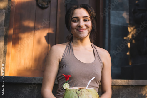 Obraz na płótnie Half length portrait of positive caucasian female recreating with organic vegan drink after yoga practice, smiling hipster girl enjoying refreshment with coco water sitting outdoors feeling harmony w salonie