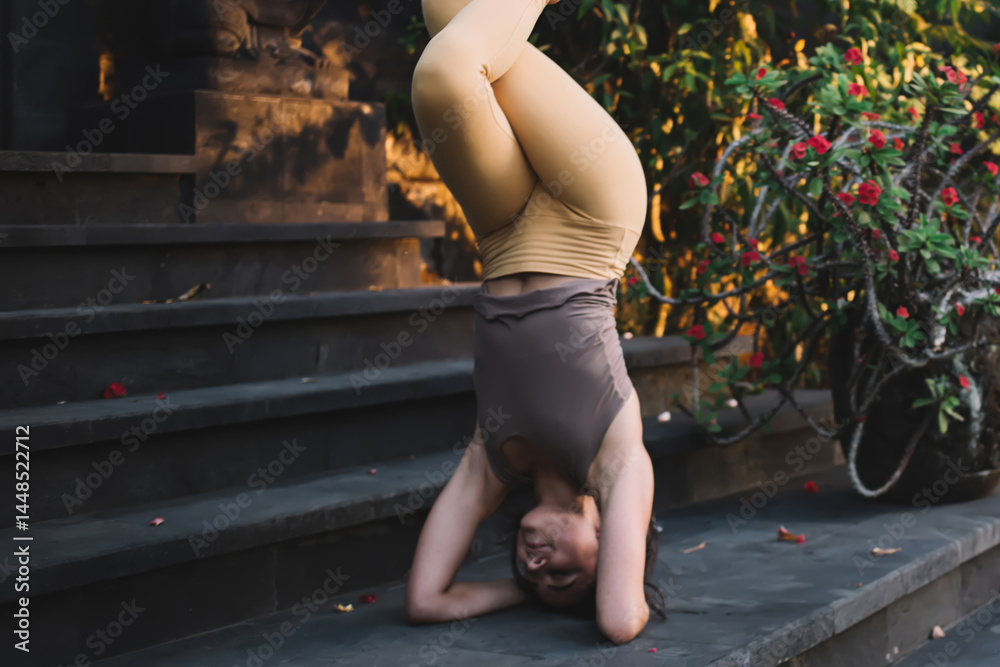 Young strong professional female in active wear enjoying inversee pose reaching balance and fit on training, positive caucasian woman satisfied with training and doing asana on stairs near retreat