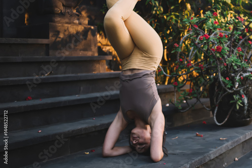 Obraz na płótnie Young strong professional female in active wear enjoying inversee pose reaching balance and fit on training, positive caucasian woman satisfied with training and doing asana on stairs near retreat w salonie