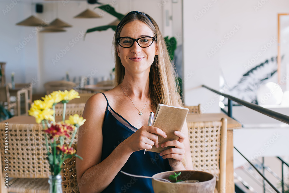 Cheerful woman with book in hands sitting in cafe
