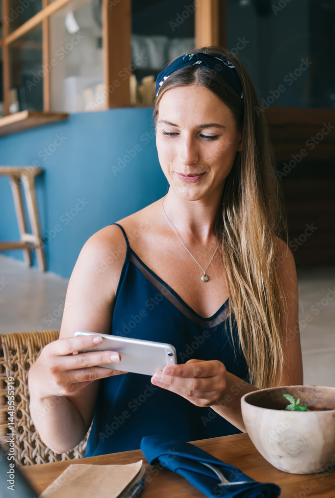 Positive woman browsing smartphone during breakfast in cafe