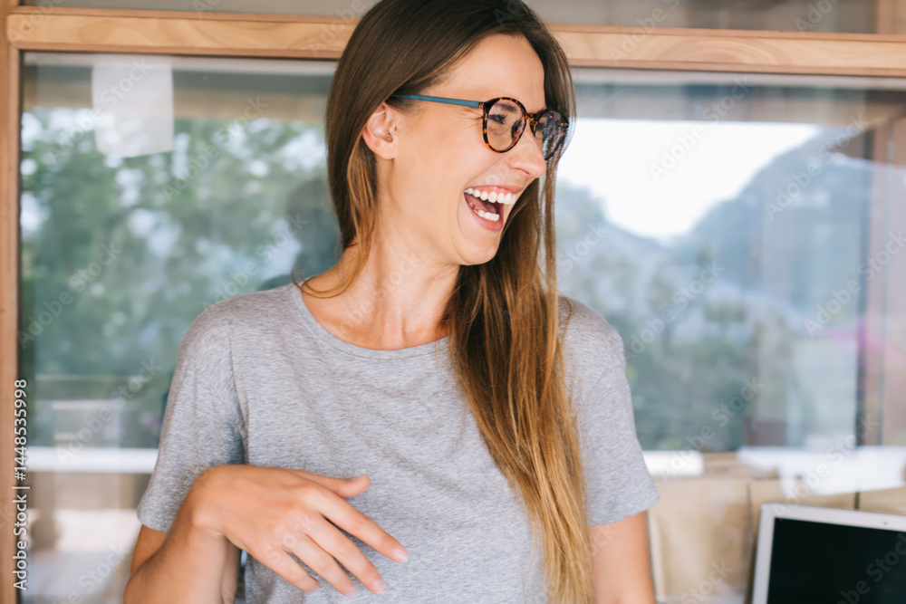 Beautiful female in gray T shirt laughing in modern workspace