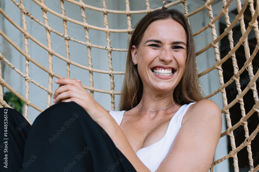Joyful young blonde resting in wicker hanging chair and laughing