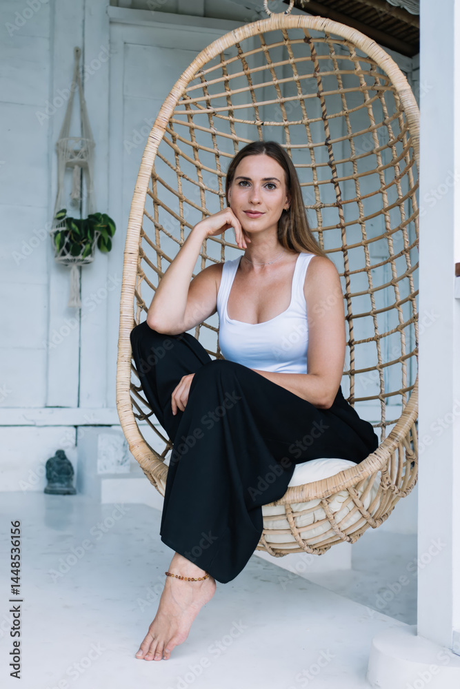 Calm thoughtful lady sitting in hanging egg chair on terrace