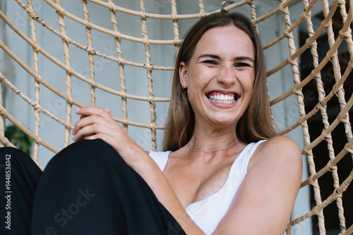 Obraz na płótnie Joyful young blonde resting in wicker hanging chair and laughing w salonie