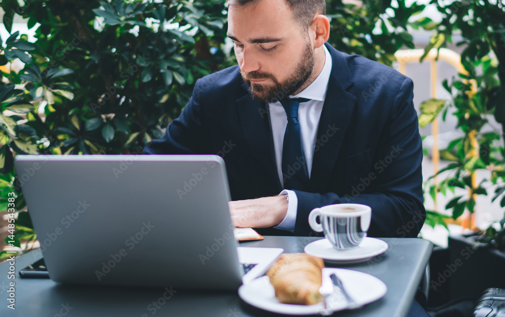 Focused young male manager working on project in garden cafe