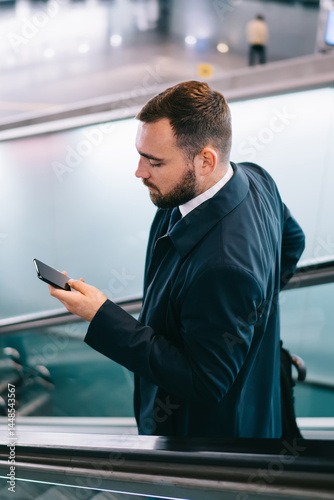 Obraz na płótnie Serious man using smartphone and standing on escalator w salonie