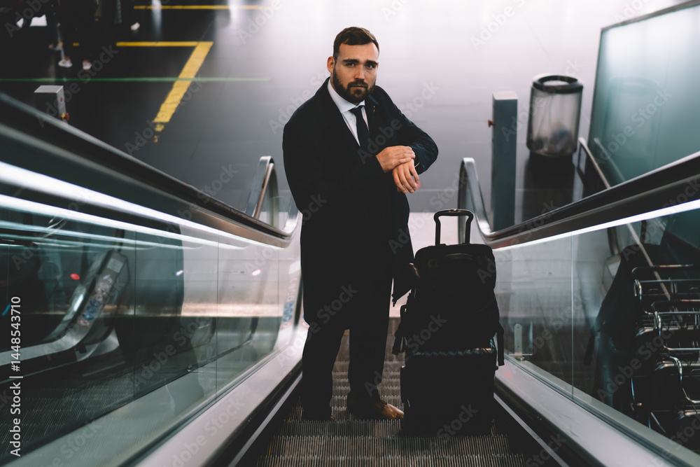 Serious businessman riding on moving stairs in airport