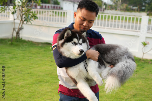 Portrait of a happy adult man enjoying time outdoors with a pet puppy Siberian Husky petting and holding a playful dog.Cheerful sport man enjoying leisure time in a garden lawn in front of the house.