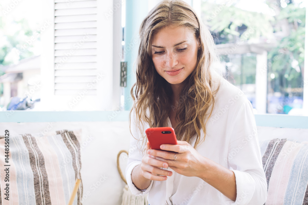 Joyful woman using smartphone while having breakfast at home