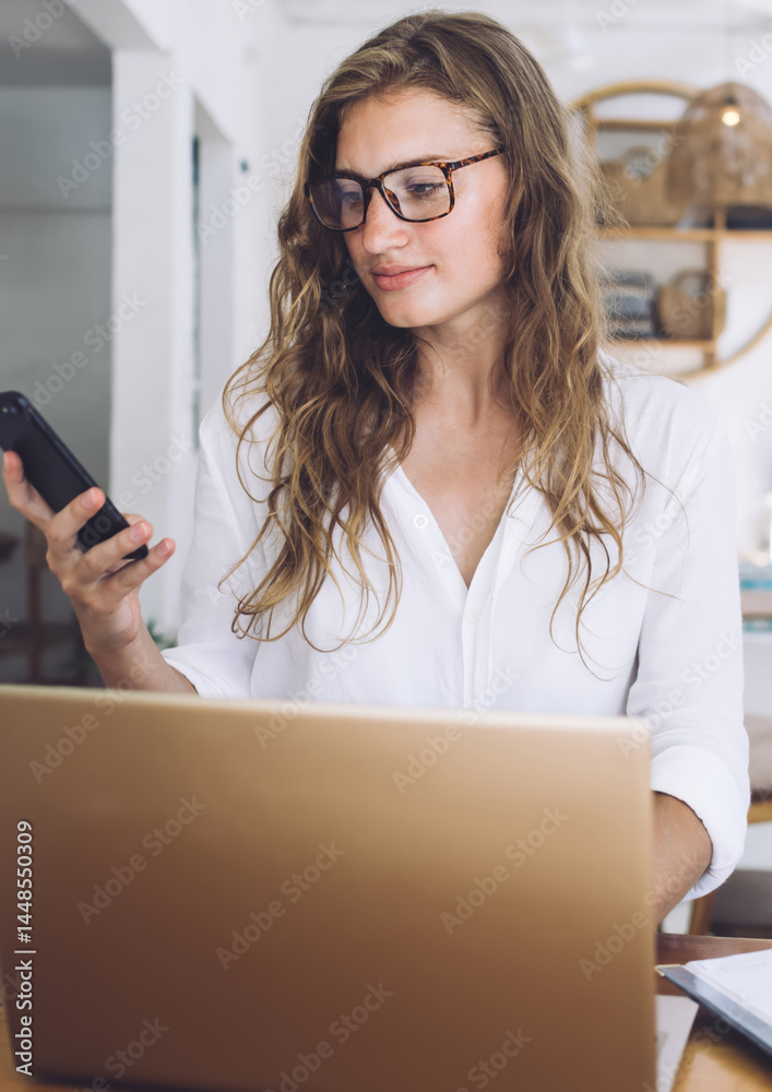 Freelancer using phone while working at laptop in cafe
