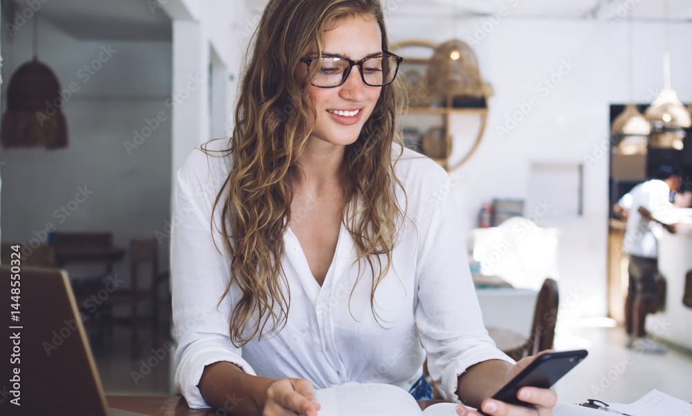 Student interacting with phone while reading book and sitting at