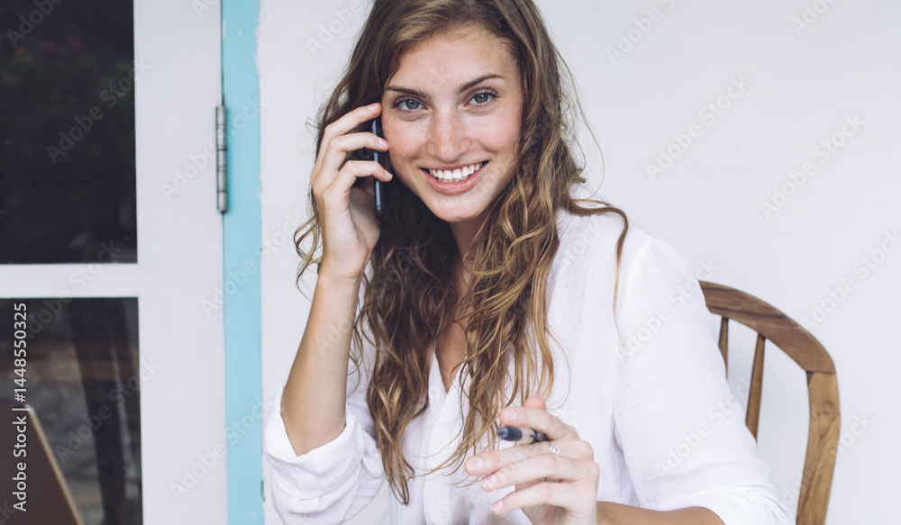 Independent cheerful woman talking on smartphone and using lapto