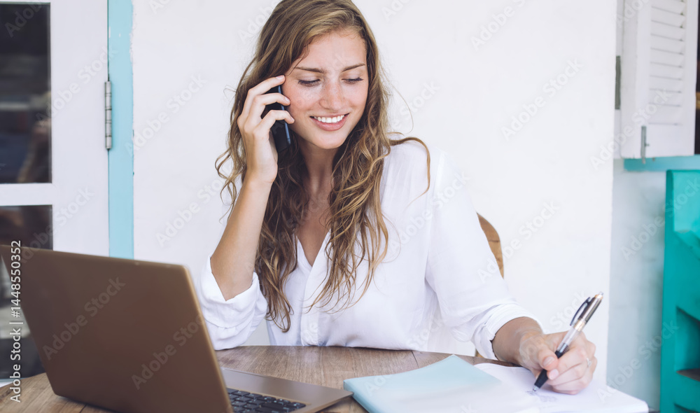 Pleasant casual businesswoman talking on smartphone and using la