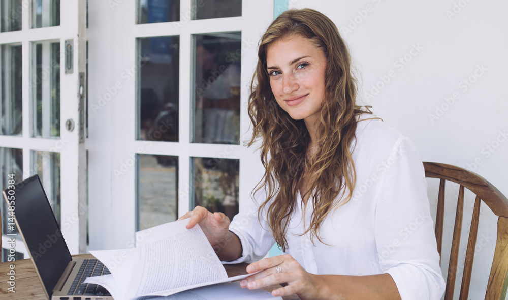 Joyful young female student scrolling through book and sitting a