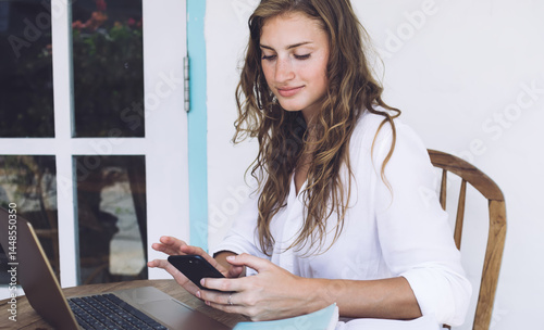 Obraz na płótnie Young woman freelancer smiling and typing on smartphone w salonie