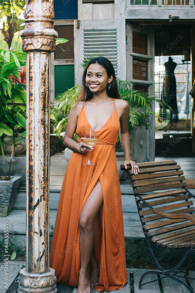 Young ethnic female tourist in maxi dress enjoying summer day in exotic cafe