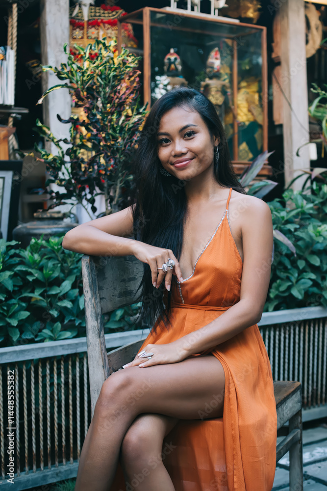 Happy young ethnic woman sitting with legs crossed in tropical cafe