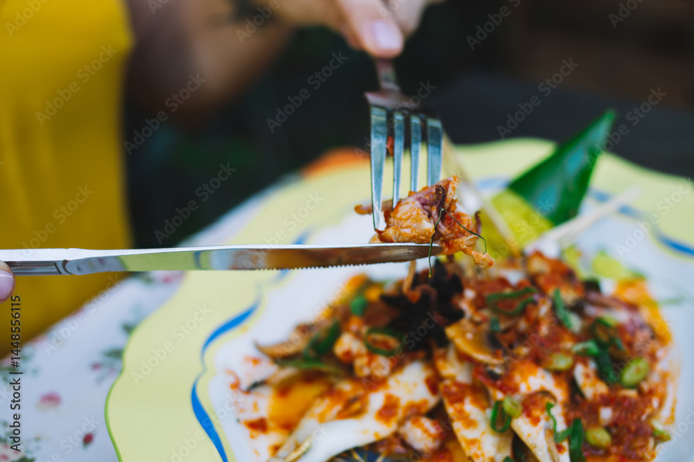 Crop woman eating seafood dish with fork and knife