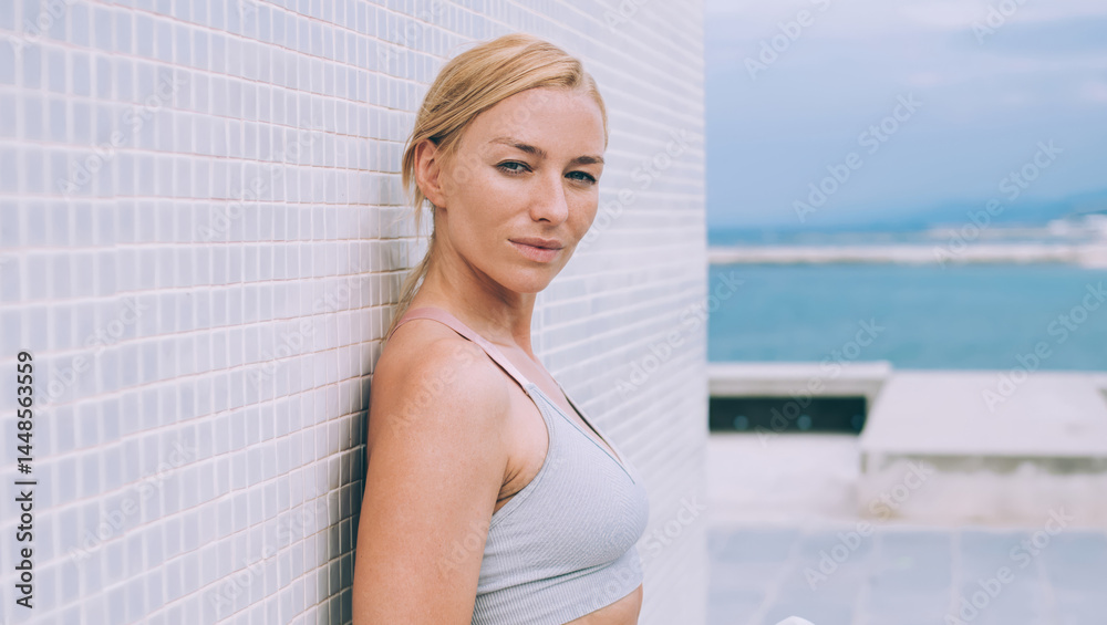 Half length portrait of attractive female dressed in trendy sportive tracksuit posing at urbanity, beautiful Caucasian jogger with water bottle in hands looking at camera during workout break