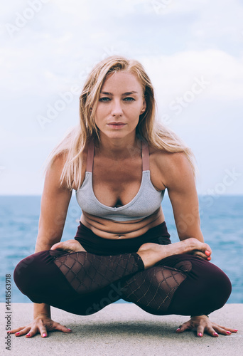 Obraz na płótnie Experienced Caucasian female standing on hands doing yoga during morning workout in nature environment near coastline, Sportswoman practicing lolasana pose enjoying healthy energy lifestyle w salonie