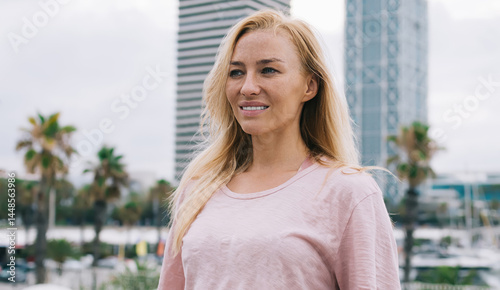 Obraz na płótnie Carefree Caucasian female tourist dressed in casual clothing standing at urban setting and smiling, charming hipster girl in stylish outfit enjoying leisure time for visiting city during solo travel w salonie