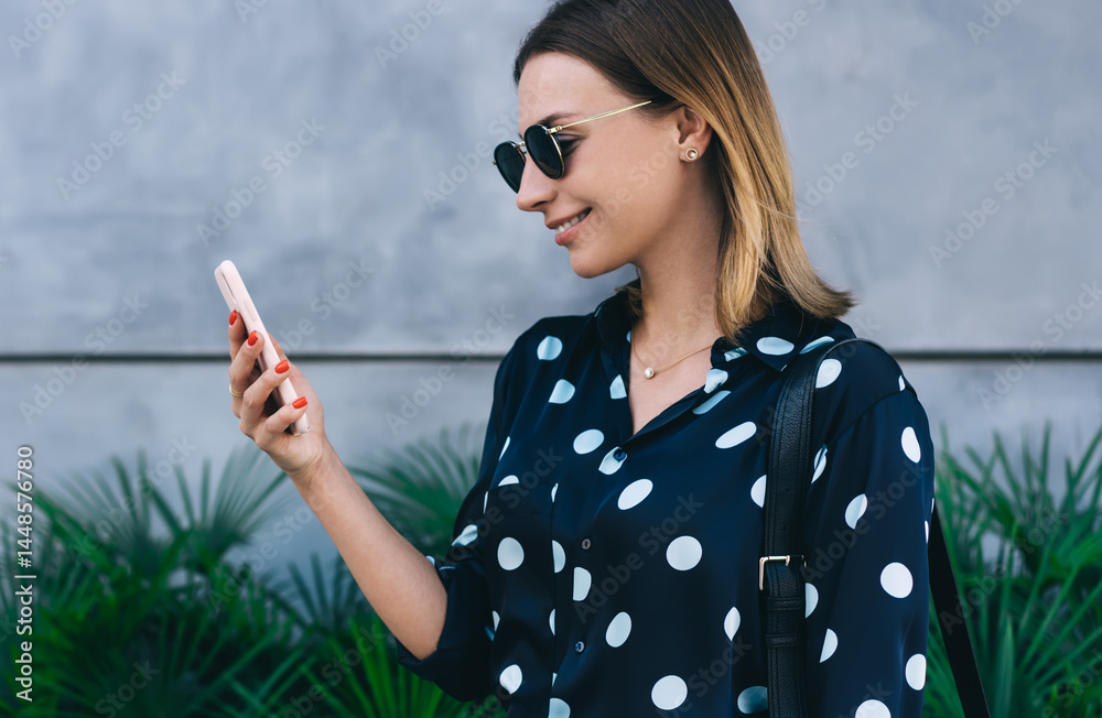 Pleased woman using smartphone while standing near greenery