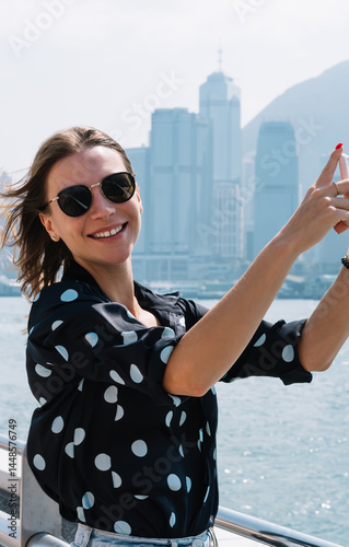 Obraz na płótnie Happy caucasian female influencer shooting video for blog using mobile phone camera exploring downtown, smiling woman in sunglasses taking photos during vacation journey hold smartphone on bridge w salonie