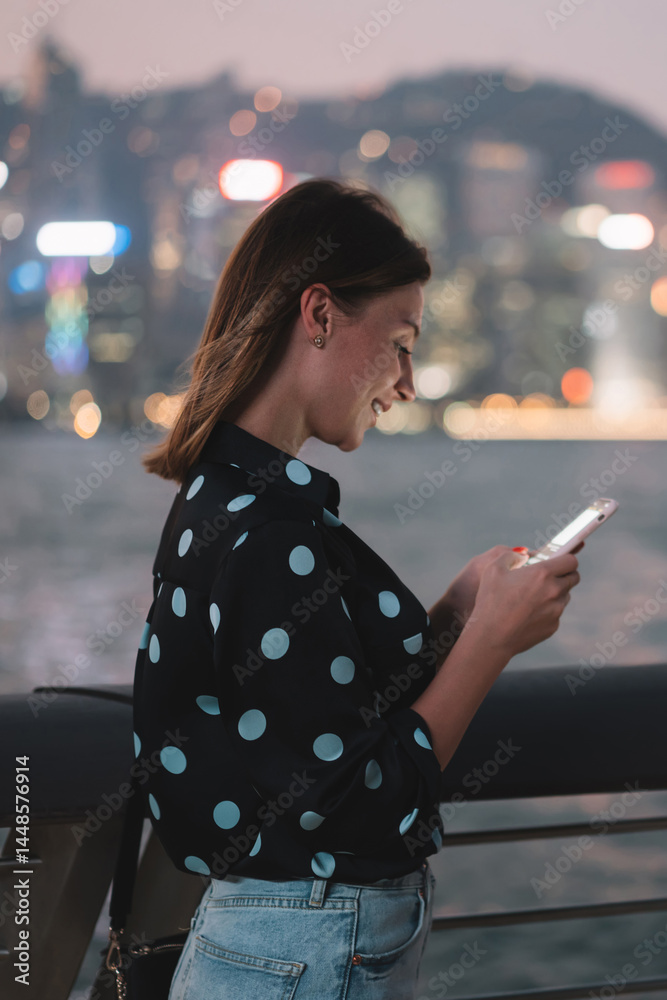 Smiling woman using smartphone on embankment in evening