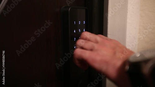  Hand enters the code on a digital door lock, unlocking the door. The smart lock combines security and convenience for home or office access.
