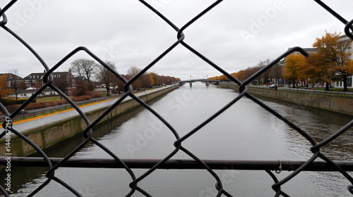 Chain-link fence along a navigable canal on a raining autumn day. Security concept.
