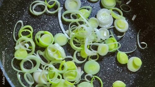 A chef stirs sliced leeks while frying them in a pan with olive oil. Slow motion video 100fps.