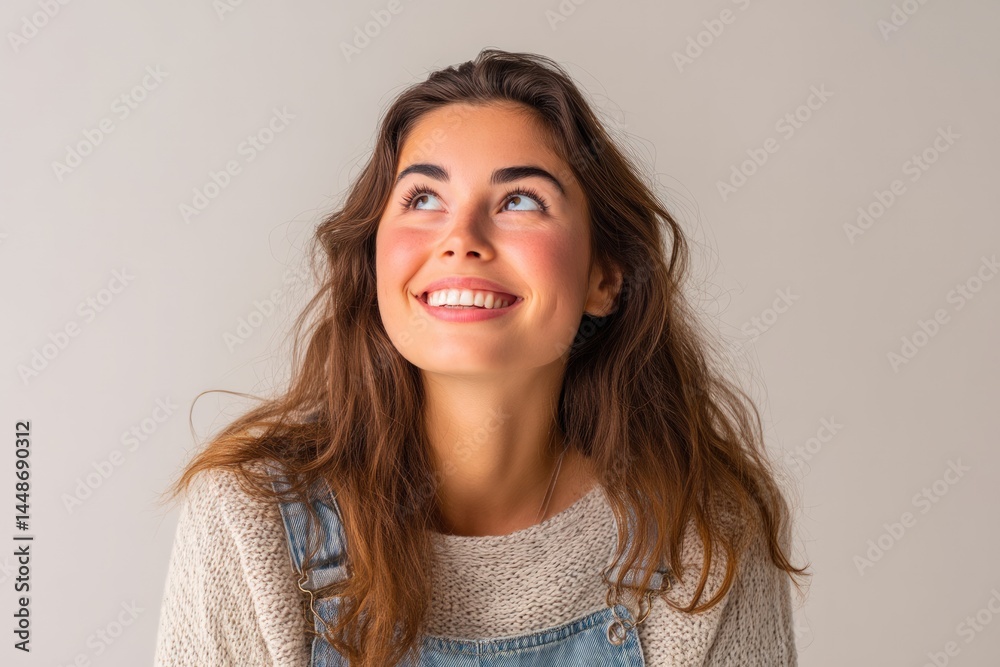 Smiling woman looks upwards, hopeful expression. Light sweater and blue overalls Smiling woman looks upwards, hopeful expression. Light sweater and blue overalls