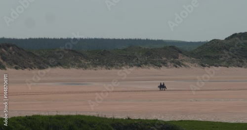 Two people walk on horses on empty large beach sand strand slow motion