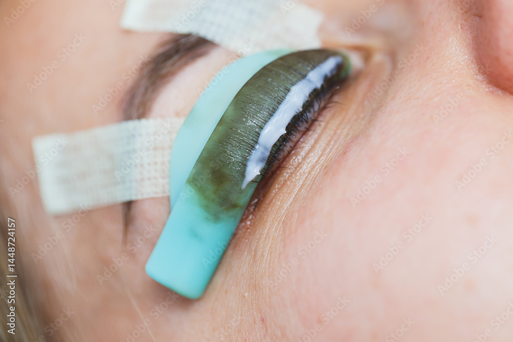 Eyelash lamination procedure on a woman's face. A cosmetologist glues long eyelashes with tweezers onto a woman's eye during an eyelash extension procedure.