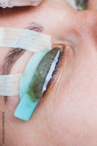 Obraz na płótnie Eyelash lamination procedure on a woman's face. A cosmetologist glues long eyelashes with tweezers onto a woman's eye during an eyelash extension procedure. w salonie