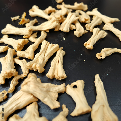A close-up of dried galangal root pieces scattered over a dark surface, emphasizing the unique shapes and the tactile quality of the texture.