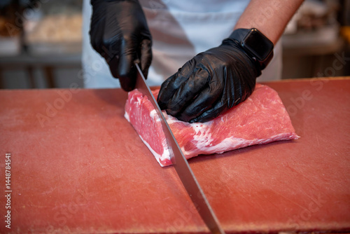 Butcher cutting fresh meat with sharp knife in butchery