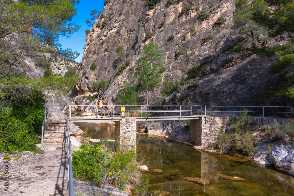 Tourists walking on bridge over canaletes river at fontcalda sanctuary in gandesa, tarragona, spain
